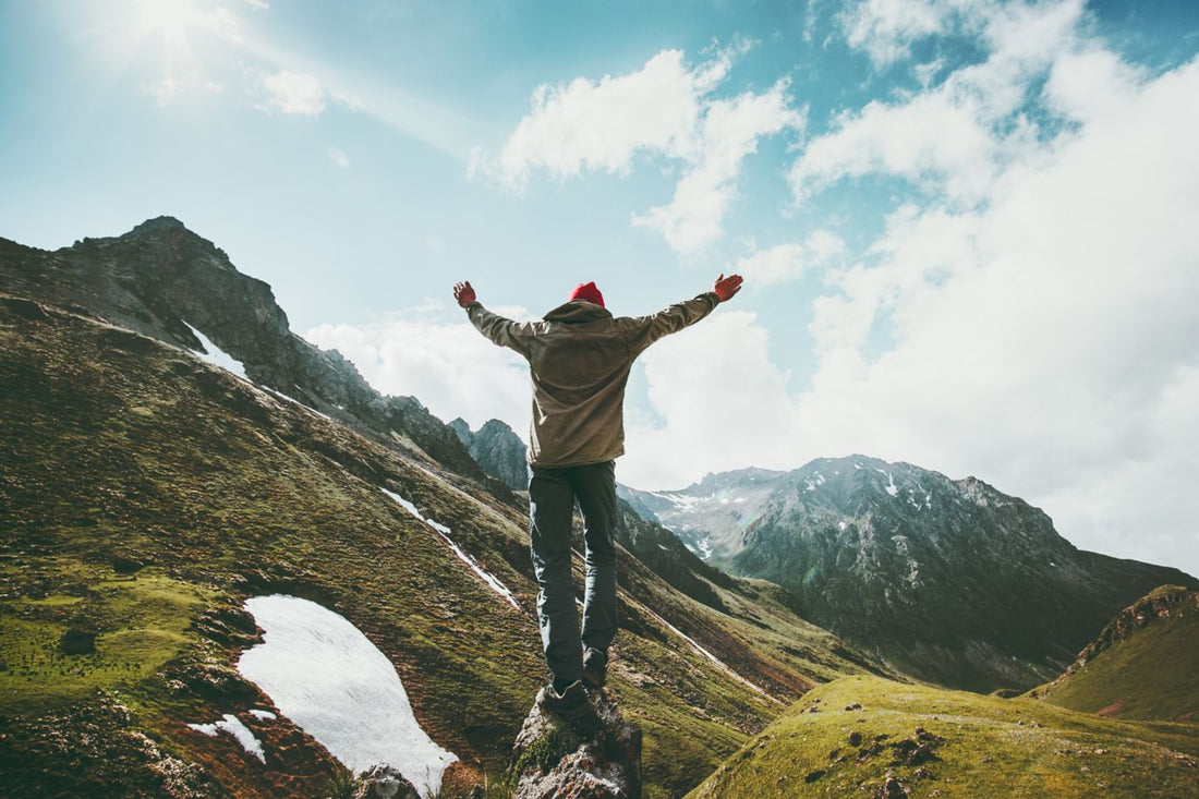 Traveler Man raised hands standing on cliff mountains