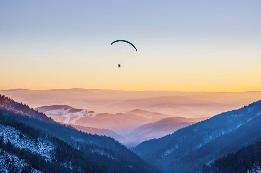 Paraglider silhouette flying over misty mountain valley in beautiful warm sunset colors