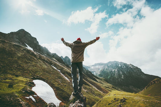 Traveler Man raised hands standing on cliff mountains