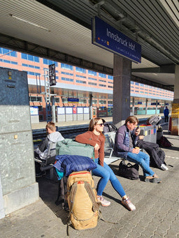 A person at a train station sitting with an Eagle Creek backpack and large duffle bag