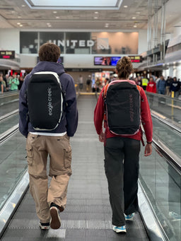 Two people walk through an airport wearing Eagle Creek duffle bags