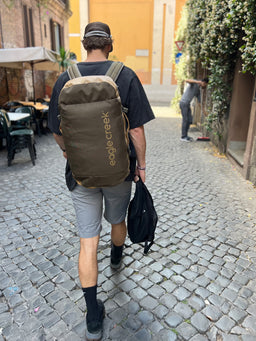 A person wearing an Eagle Creek duffle bag walking in an alley