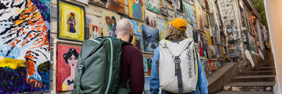 Two people look at art while wearing Eagle Creek Tour Travel Backpacks