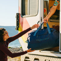 A person in a camper passes a navy blue duffle bag to outstretched arms