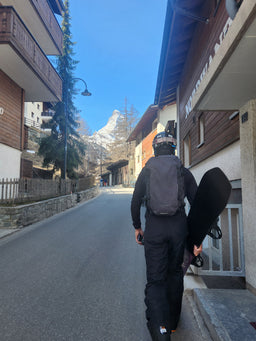 A person carrying a snowboard and wearing an Eagle Creek backpack walking down a street