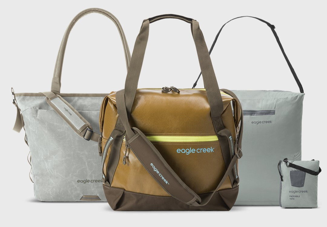 Three Eagle Creek travel bags, including a gold duffel and two gray packable totes.