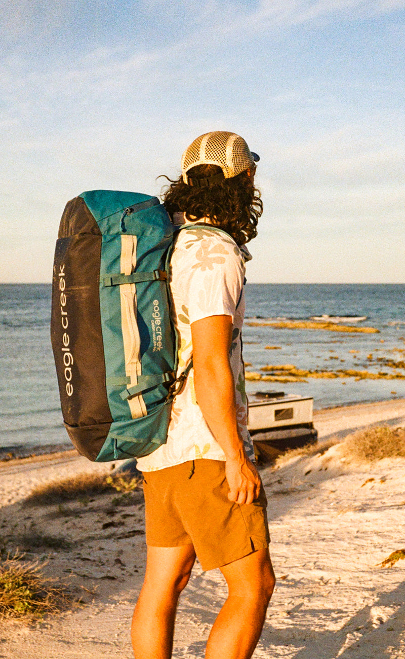 A man standing in a train terminal wearing a large white travel backpack.