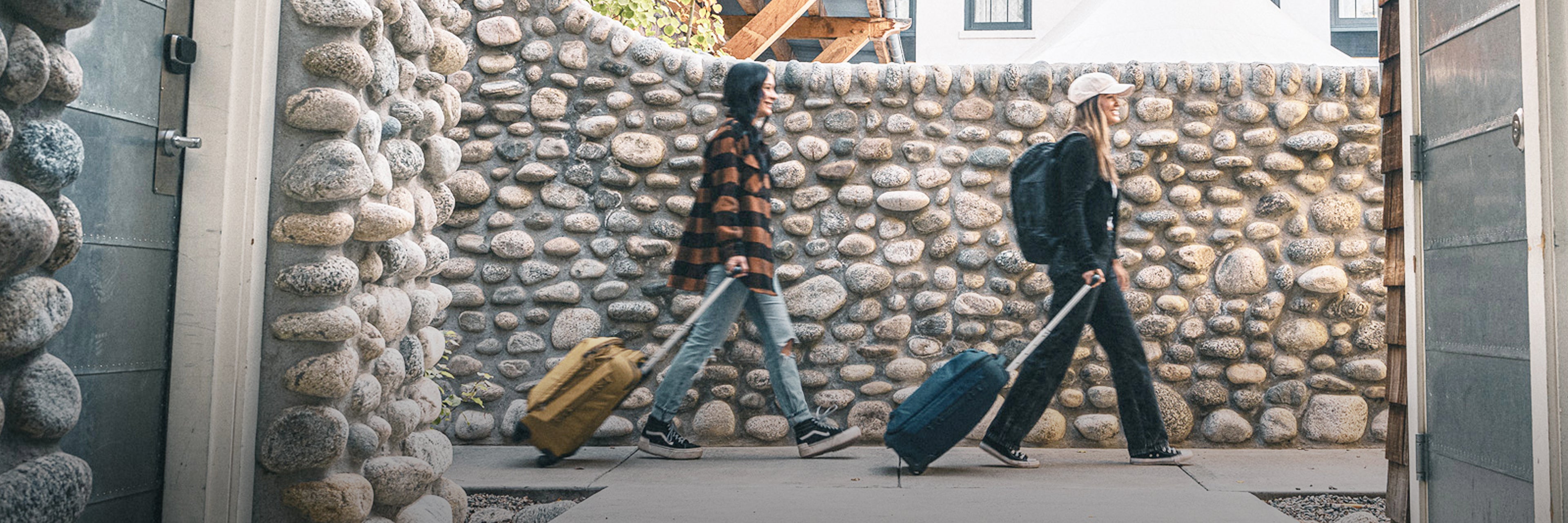 Two women roll their luggage in an alleyway