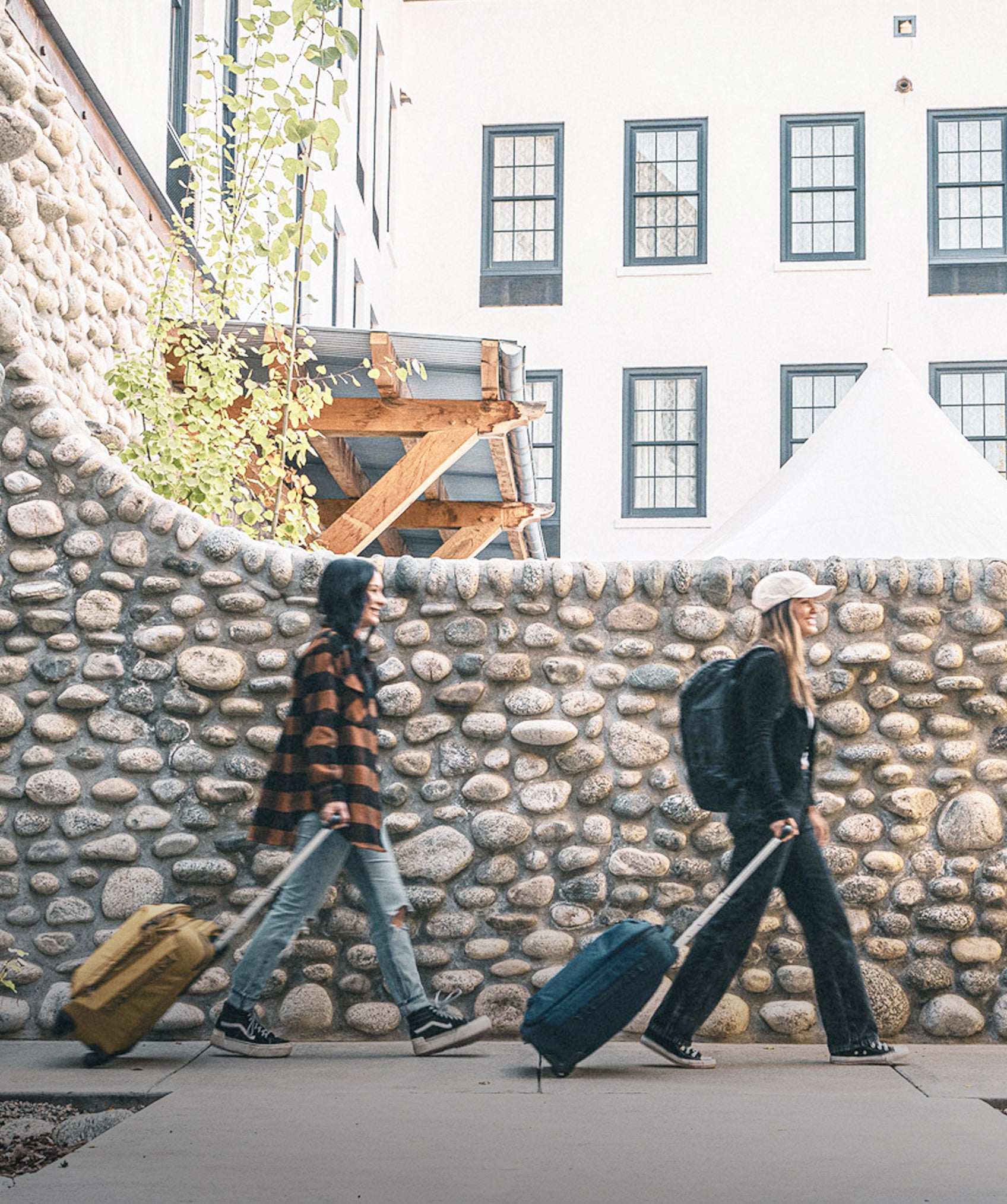 Two women roll their luggage in an alleyway