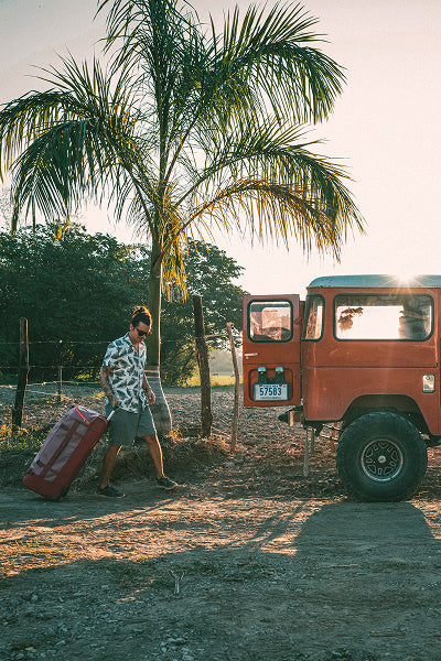 A man pulls a bag towards a truck in a tropical setting.