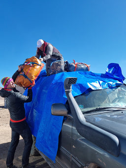 Two people loading Eagle Creek duffle bags onto a car with a blue tarp.