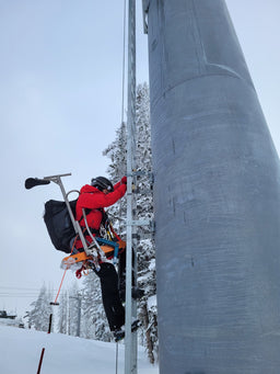 A ski patroller climbs a lift tower wearing an Eagle Creek duffle bag
