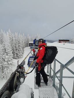 A ski patroller stands on top of a gondola wearing an Eagle Creek duffle bag