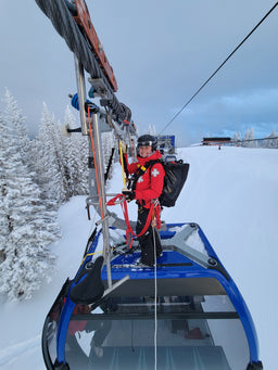 A ski patroller stands on top of a gondola cabin wearing an Eagle Creek duffle bag