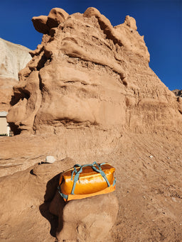 An orange Eagle Creek duffle bag on a rock in the desert