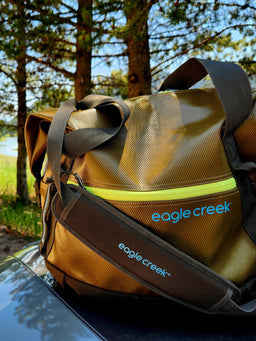 A brown Eagle Creek tote bag in the woods