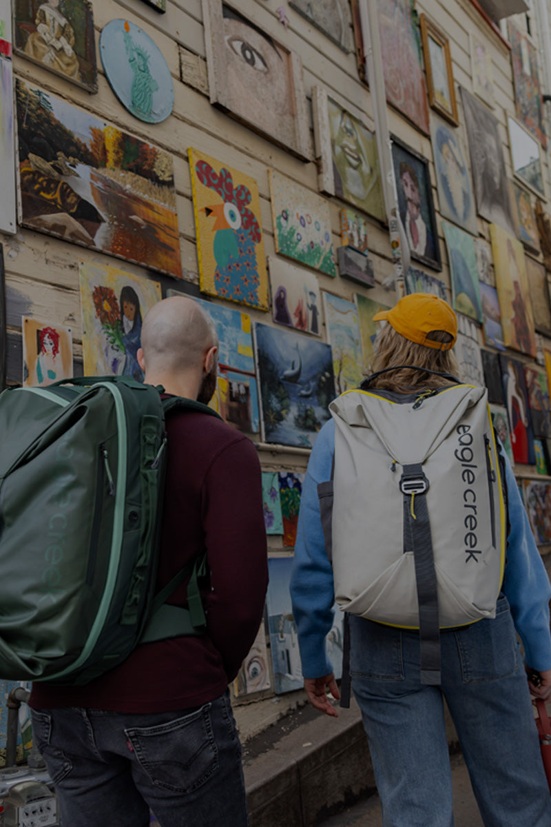 Two people look at art while wearing Eagle Creek Tour Travel Backpacks