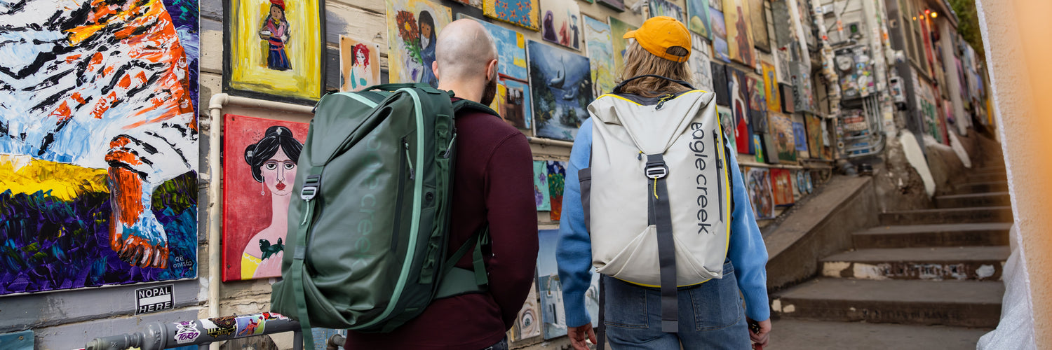 Two people admiring artwork while wearing Eagle Creek travel backpacks