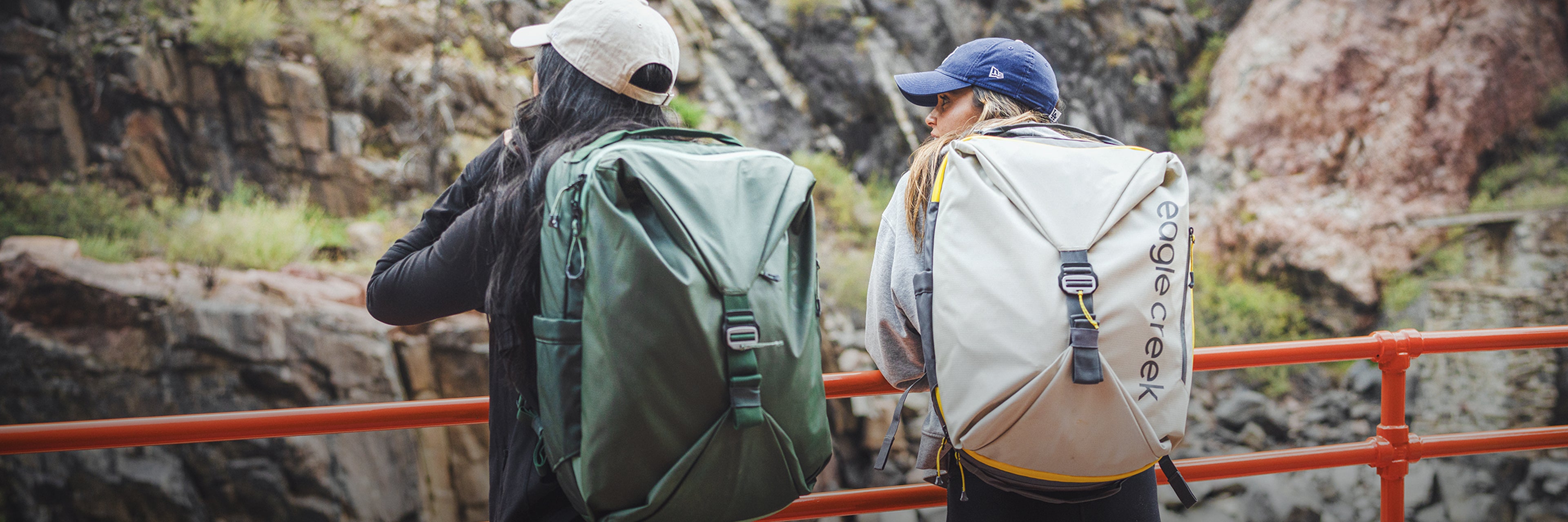 Two women on a bridge wearing new Tour Travel Backpacks look out over a canyon