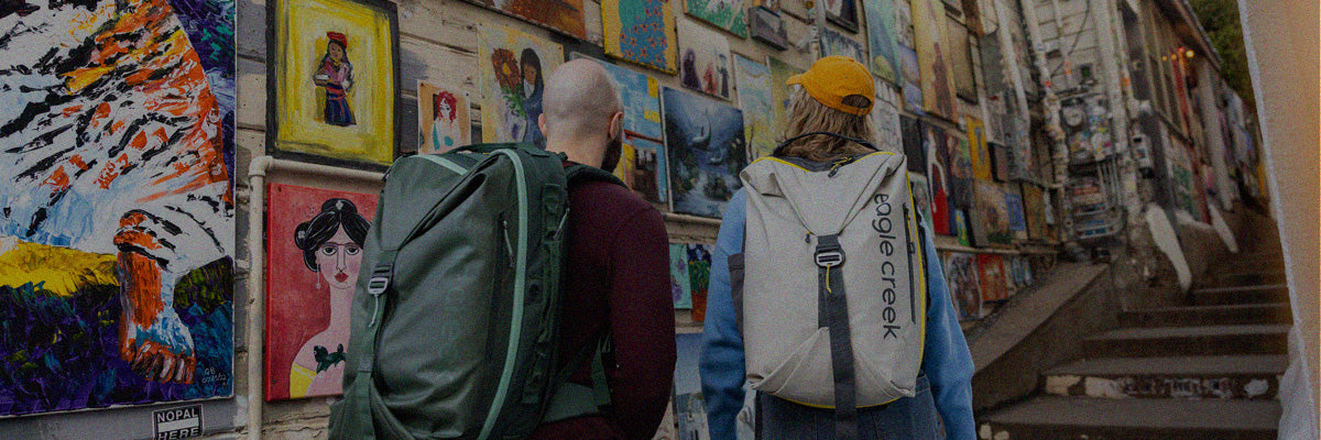 Two people look at art while wearing Eagle Creek Tour Travel Backpacks